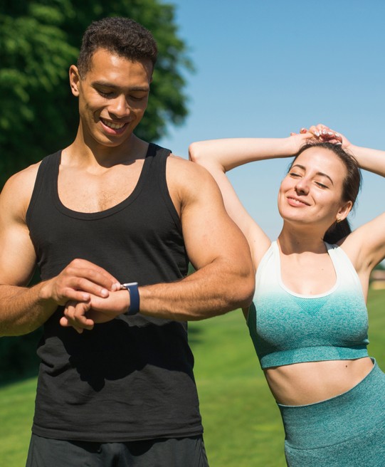 man looking at his wrist watch while women beside him is happily exercising